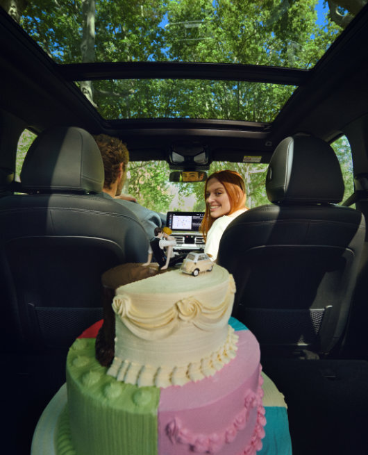 Customer seated inside of a BMW iX3 M looking into the back seat. A wedding cake is seated in the middle of the car.