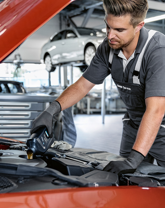 BMW Service employee pouring Original BMW Engine Oil into a BMW vehicle engine.